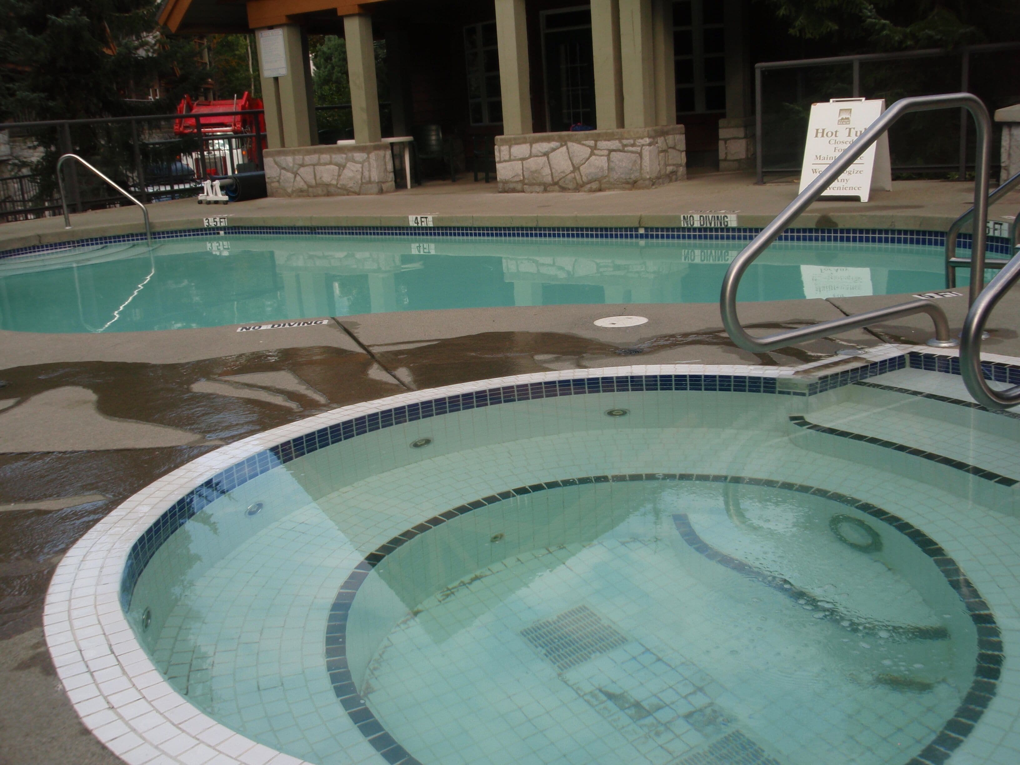 Une piscine avec un panneau indiquant qu’il est interdit de plonger, un mur de pierre et un espace abrité surmonté d’un toit rouge.