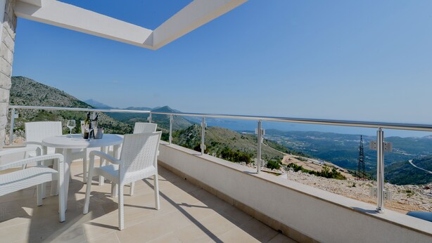 A terrace with white wicker furniture, a table with wine bottles, and a scenic view of the landscape. - Dubrovnik Sea Views (Ravno)
