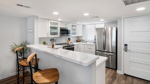 Una cocina moderna con armarios blancos, electrodomésticos de acero inoxidable, una isla central con taburetes altos y piso de madera.