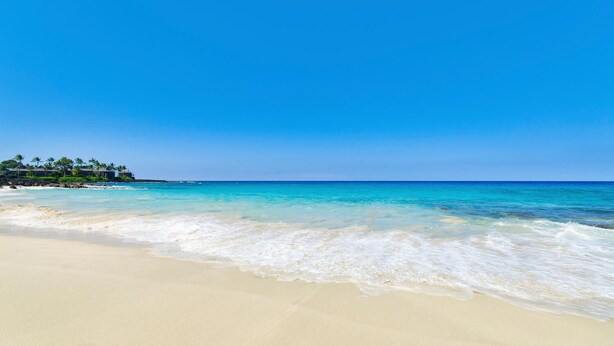 Una playa con agua turquesa cristalina, arena blanca y un resort con palmeras al fondo.