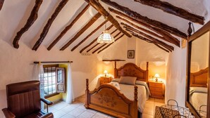 A bedroom with a wooden bed, two bedside tables with lamps, a chair, and a window with a curtain. - Casa Rural La Cañada Villanueva de Algaidas by Ruralidays (Málaga)