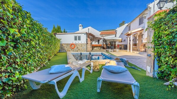 A poolside area with two sun loungers, a stone wall, and a clear blue sky.