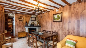 A rustic dining area with a stone fireplace, wooden beams, and a yellow sofa.