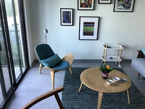 A modern living room with a teal chair, a wooden coffee table, and a small white shelf with a vase of flowers.