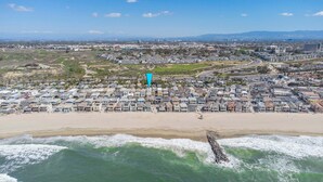 An aerial view of a coastal residential area with houses, a beach, and a road leading to a larger town.