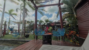 An outdoor seating area with wooden deck, metal chairs, and a thatched roof structure.