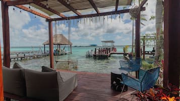Een houten terras met uitzicht op de oceaan en een gebouw met rieten dak.