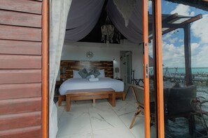 A bedroom with a wooden bed, a nightstand, and a view of the ocean. - Blue Bird Hotel Boutique (Bacalar)