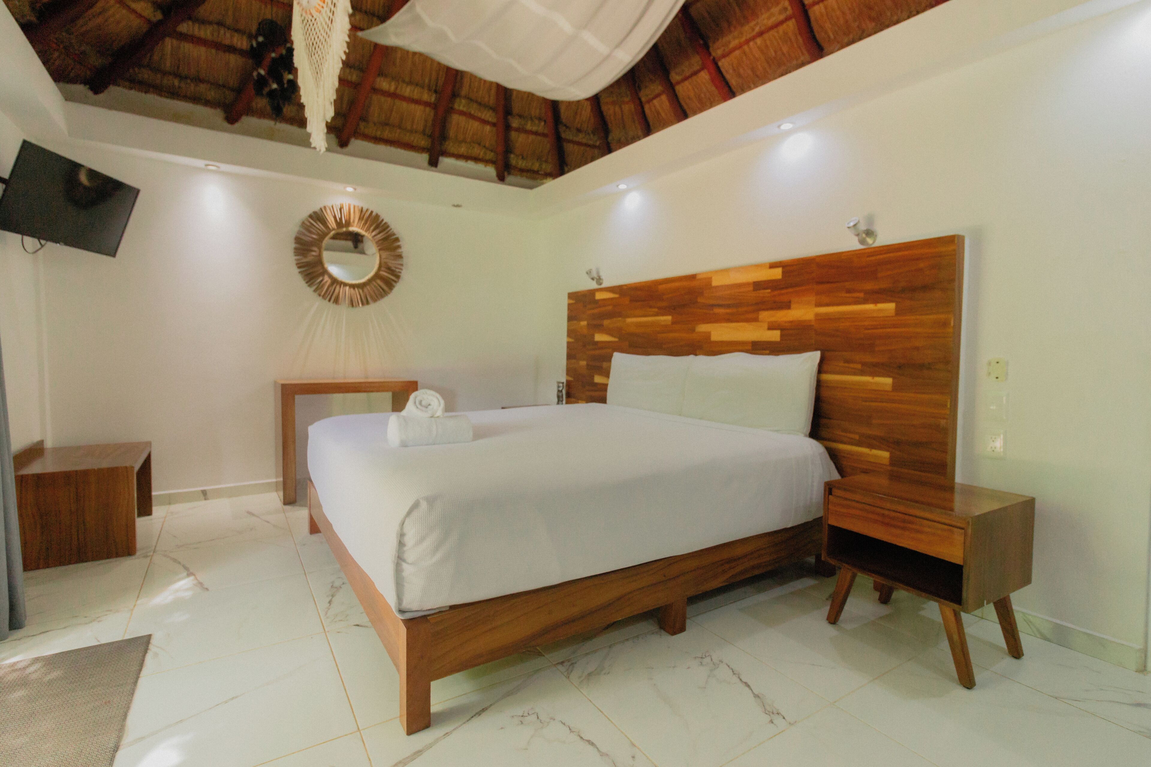 Een slaapkamer met een houten hoofdbord, een bed met wit beddengoed, een nachtkastje, een aan de muur bevestigde televisie en een plafondventilator.