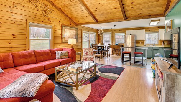 A spacious living area with a red sofa, a glass coffee table, and a wooden ceiling. - High Peak Heaven: Cozy Log Cabin on 1 Acre! (Windham)
