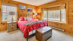 A wooden cabin bedroom with a bed, bedside tables, and a window with a view of trees. - High Peak Heaven: Cozy Log Cabin on 1 Acre! (Windham)