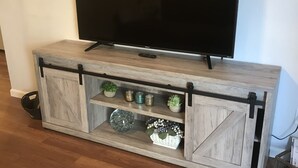 Ein Holz-Unterhaltungsschrank mit einem Flachbildfernseher auf der Oberseite, mit offenen Regalen und dekorativen Gegenständen sowie einer Schiebetür.