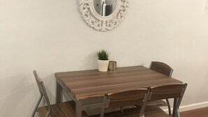 Ein Essbereich mit Holztisch und Metallstühlen, einem dekorativen Spiegel und einem kleinen Topfpflanzen an der Wand.