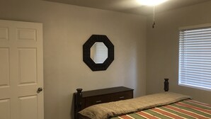 Ein Schlafzimmer mit Bett, Schminktisch, Deckenventilator, Fenster mit Jalousien und einer Tür.