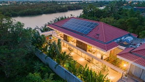 Une maison moderne avec un toit rouge, des panneaux solaires et une vue sur une rivière.