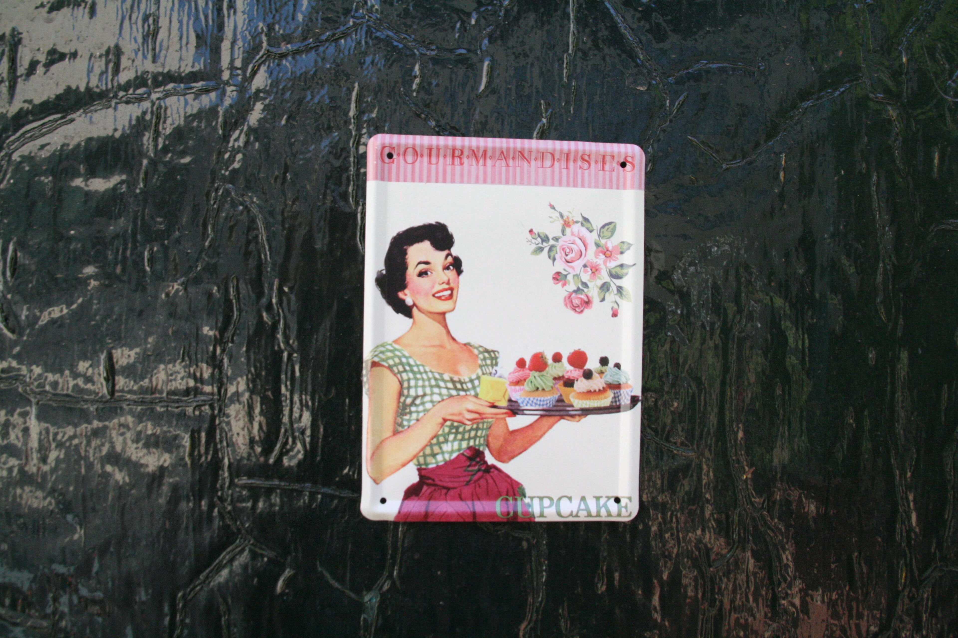 Una señal de estilo vintage con una mujer sosteniendo una bandeja de cupcakes, sobre un fondo oscuro y con textura.