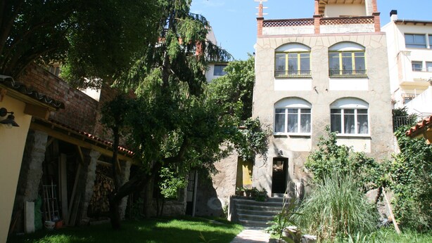 Un edificio de dos pisos con fachada de piedra, ventanas amplias y una chimenea de ladrillo.