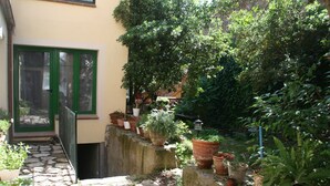 Un sendero de piedra conduce a una puerta verde, rodeada de macetas con plantas y un jardín exuberante.