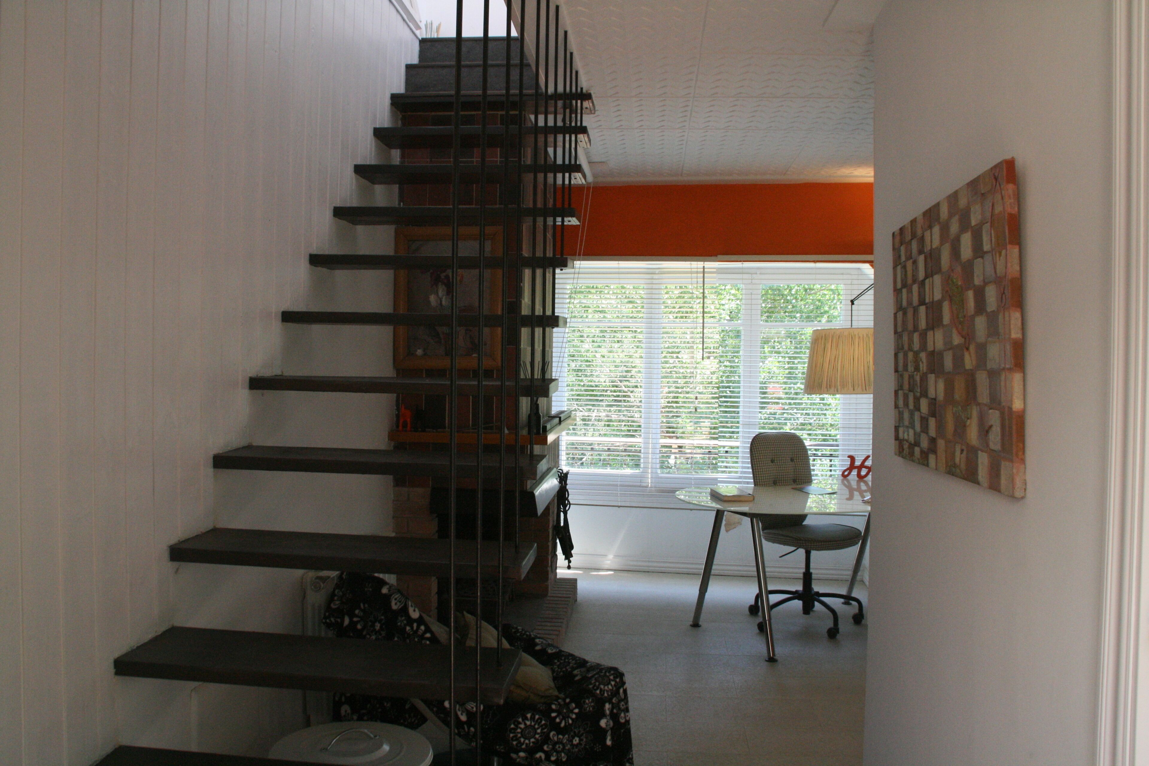 Una escalera que lleva al segundo piso, un comedor con mesa y silla, y un ventanal con persianas.