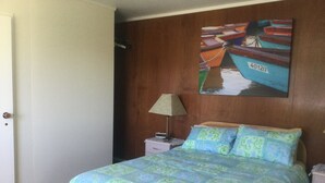 A bedroom with a bed, a nightstand, a lamp, a painting, and a door.
