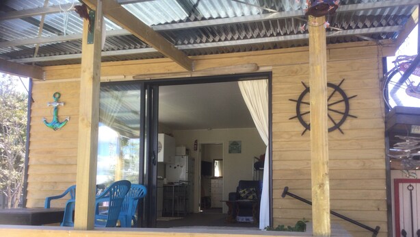 A wooden structure with a covered patio area, a sliding glass door leading to an interior space, and nautical-themed decor including an anchor and a ship's wheel.