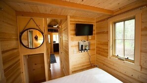 Ein Zimmer einer Holzhütte mit einem Bett, einem an der Wand befestigten Fernseher und einem Fenster.