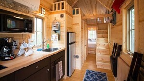 Eine kompakte Küche mit Mikrowelle, Spüle und Kühlschrank, Holzvertäfelung und einer sichtbaren Treppe zu einer weiteren Ebene.