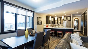 A modern kitchen with dark cabinets, a central island, and a dining area with a table and chairs. - Modern Townhome in Central Location with Private Hot Tub & Luxury Amenities! (Park City)