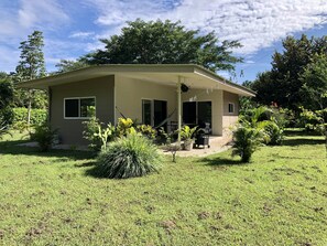 A single-story house with a covered porch, a sliding glass door, and a small garden area with various plants. - Modern and bright bungalow, tucked away, nature all around (Tamarindo)