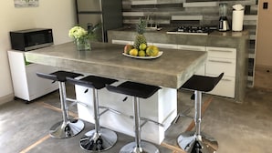 Una cocina moderna con una isla central, taburetes de bar, un refrigerador, un microondas y un frutero.