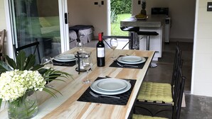 Un comedor con una mesa larga dispuesta para cuatro, una botella de vino y un florero con flores.