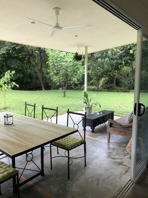 An outdoor patio with a table and chairs, a ceiling fan, and a view of a lush garden. - Modern and bright bungalow, tucked away, nature all around (Tamarindo)