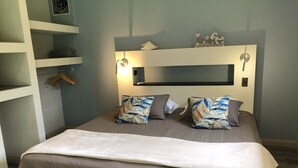 Una cama bien hecha con cabecera, una mesita de noche y un mueble auxiliar con perchero.