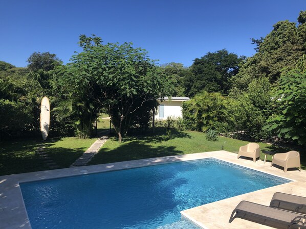 A swimming pool with a surrounding garden and a pathway leading to a building. - Modern and bright bungalow, tucked away, nature all around (Tamarindo)
