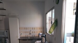 A compact kitchen with a sink, microwave, and a small refrigerator. There is a dining table with two chairs and a decorative vase. - House 2 people with sea view 15 minutes from the beach, (São José)