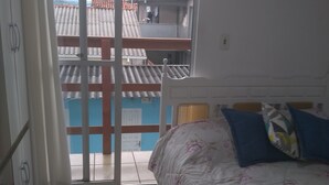 A bedroom with a bed, a sliding glass door leading to a balcony, and a bathroom with a scale. - House 2 people with sea view 15 minutes from the beach, (São José)