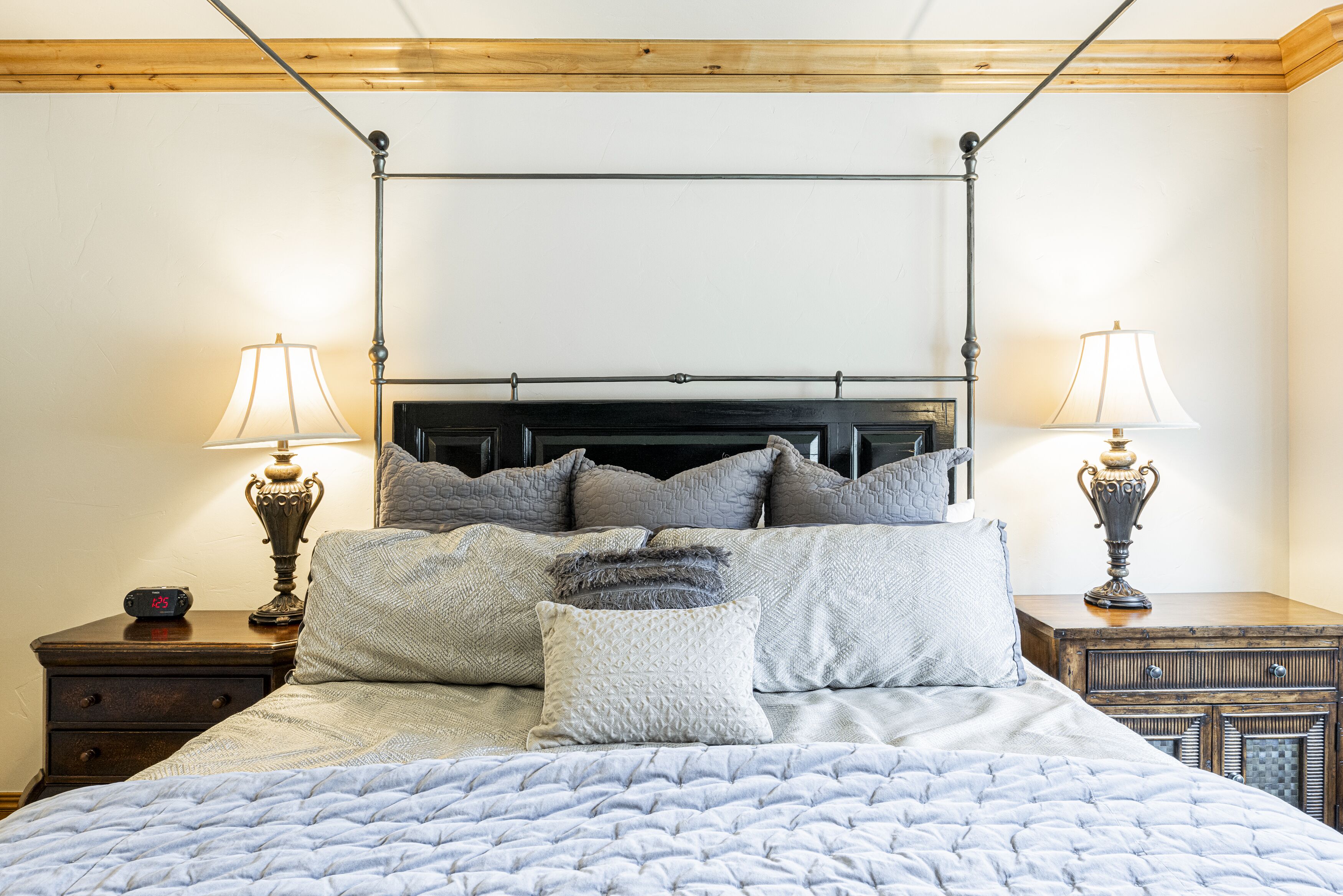 Una cama bien hecha con cabecera, dos mesitas de noche con lámparas y un cabecero de madera.