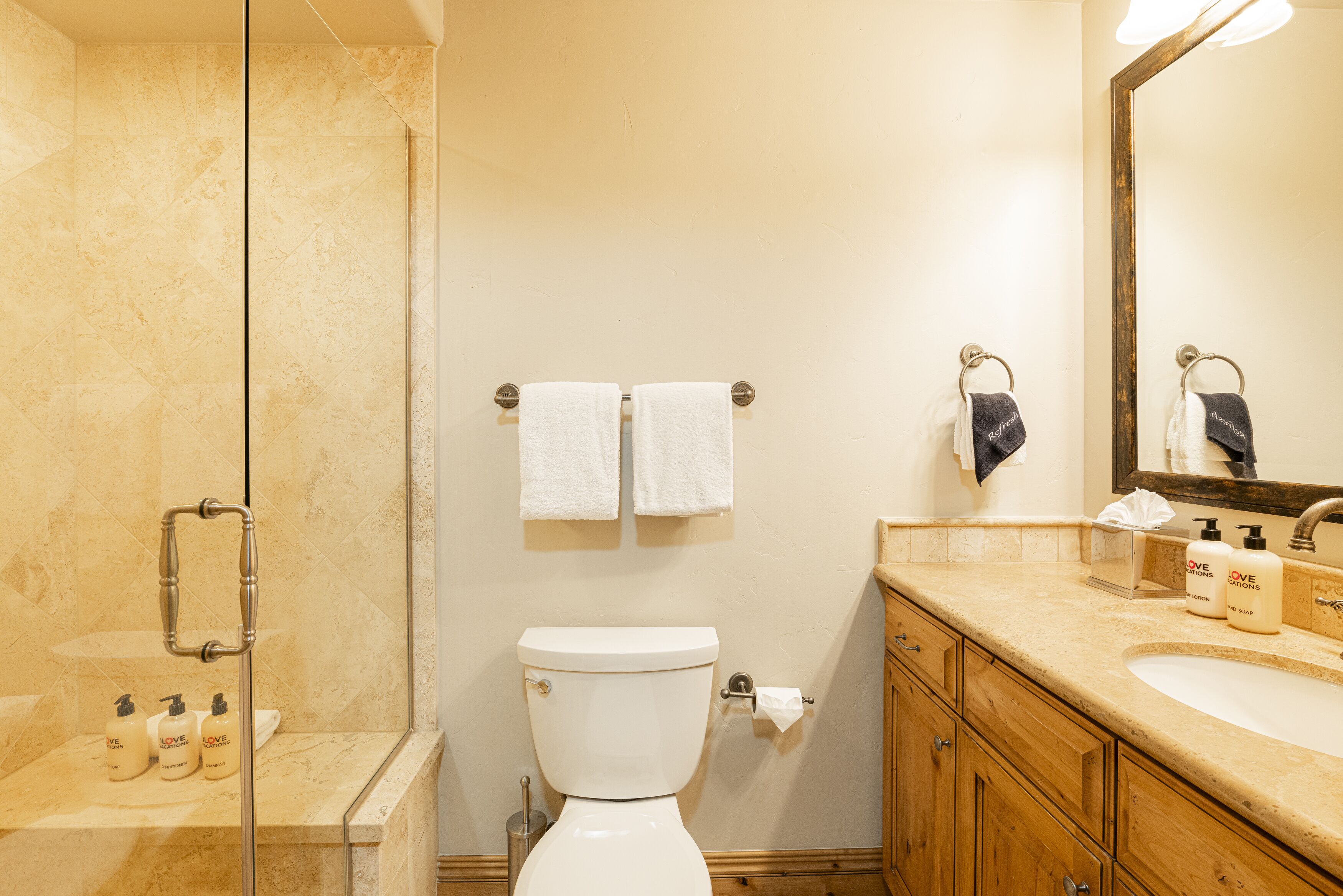 Un baño con cabina de ducha de vidrio, inodoro, lavabo con artículos de aseo y armarios de madera.