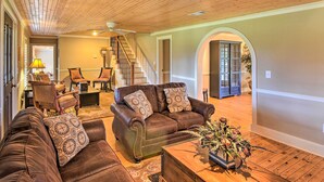 A spacious living room with a brown leather sofa set, a coffee table with a floral arrangement, and a staircase leading to another level. - Serving Southern Charm at this Clarkesville House! (Clarkesville)