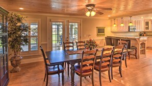 A dining area with a wooden table and chairs, a ceiling fan, and a view of the outdoors through large windows. - Serving Southern Charm at this Clarkesville House! (Clarkesville)