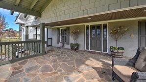 A covered patio with stone flooring, a wicker chair, and potted plants. - Serving Southern Charm at this Clarkesville House! (Clarkesville)