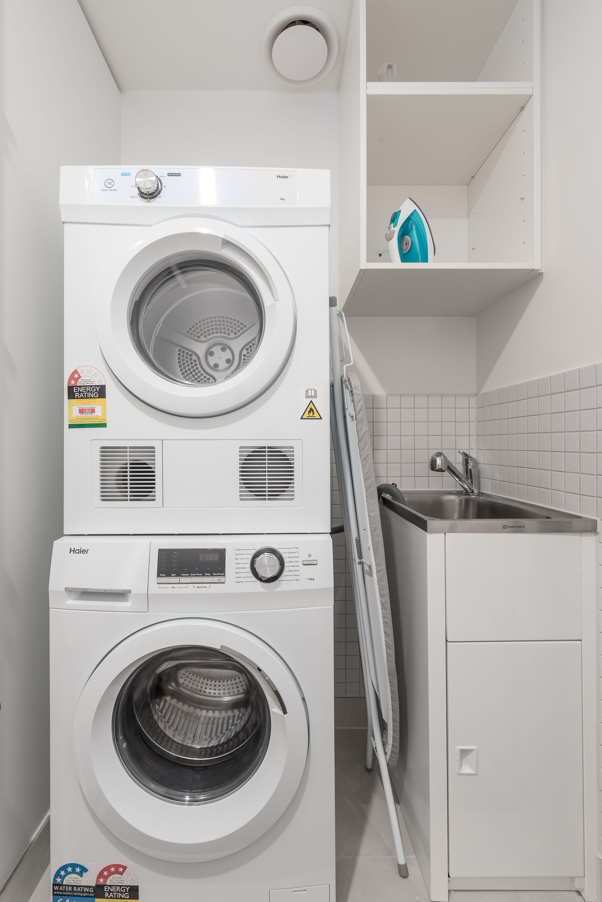Un espace buanderie compact comprenant deux machines à laver superposées et un étendoir.
