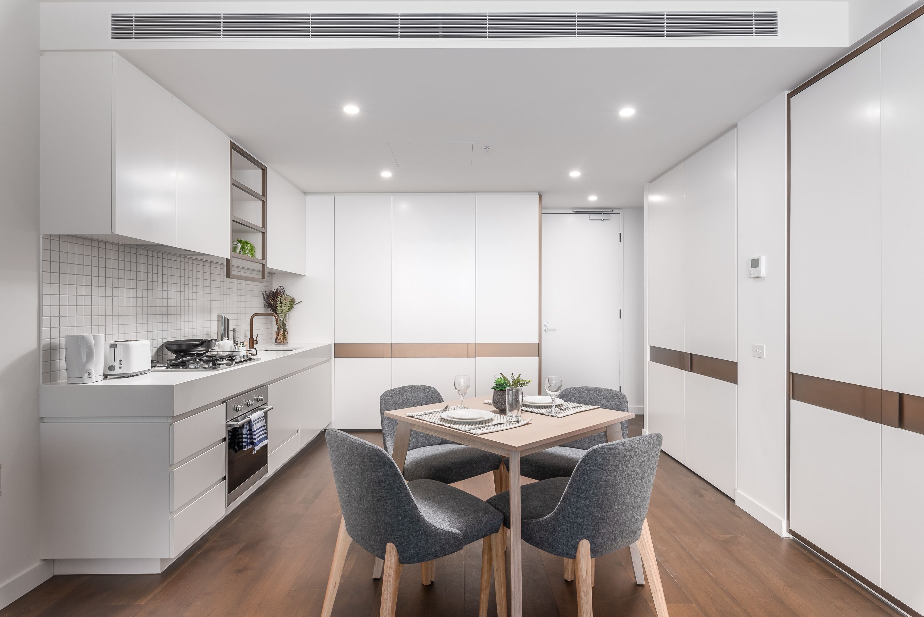 A modern kitchen with white cabinets, a dining table with four chairs, and a built-in oven.