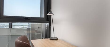 A modern office space with a wooden desk, a black desk lamp, and a clear view of the cityscape through a large window.