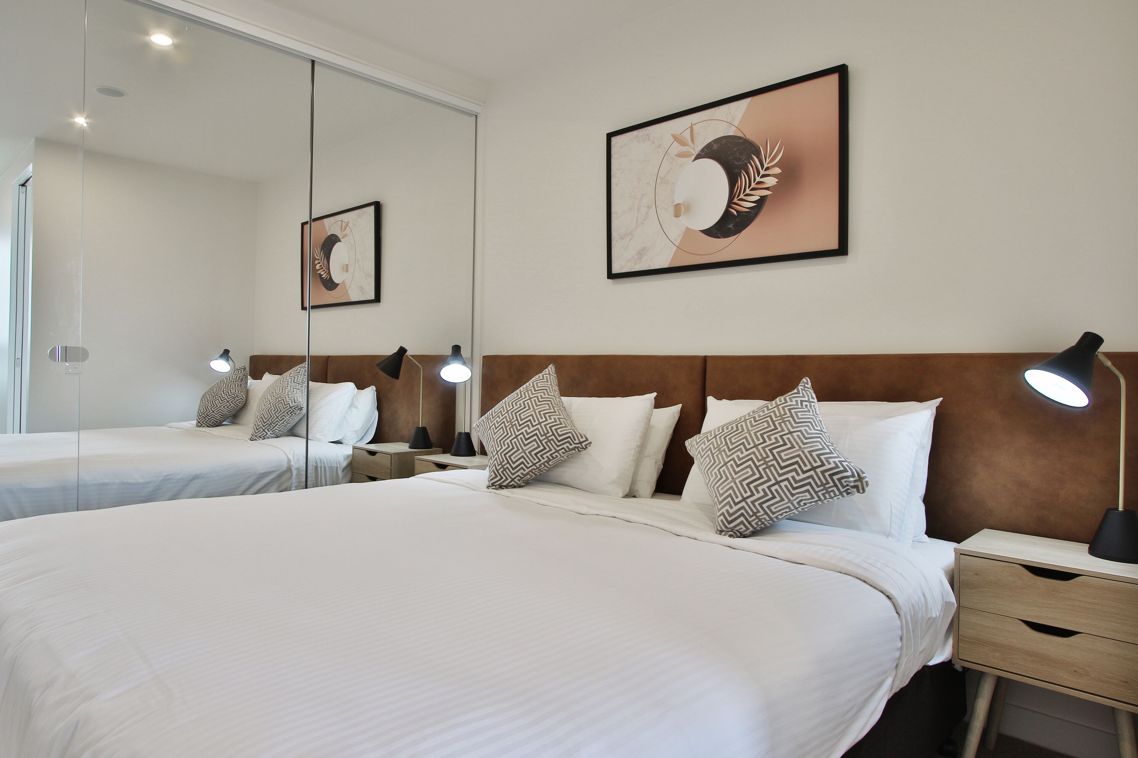 Habitación de hotel con dos camas, un cabecero de madera, un espejo grande y dos mesitas de noche con lámparas.