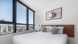 A hotel room with a large bed, a headboard, a nightstand, a lamp, and a framed picture on the wall. - Domi Serviced Apartments (Glen Waverley)