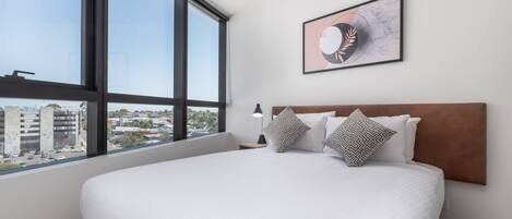 Ein Hotelzimmer mit einem großen Bett, einem Kopfteil, einem Nachttisch, einer Lampe und einem gerahmten Bild an der Wand.