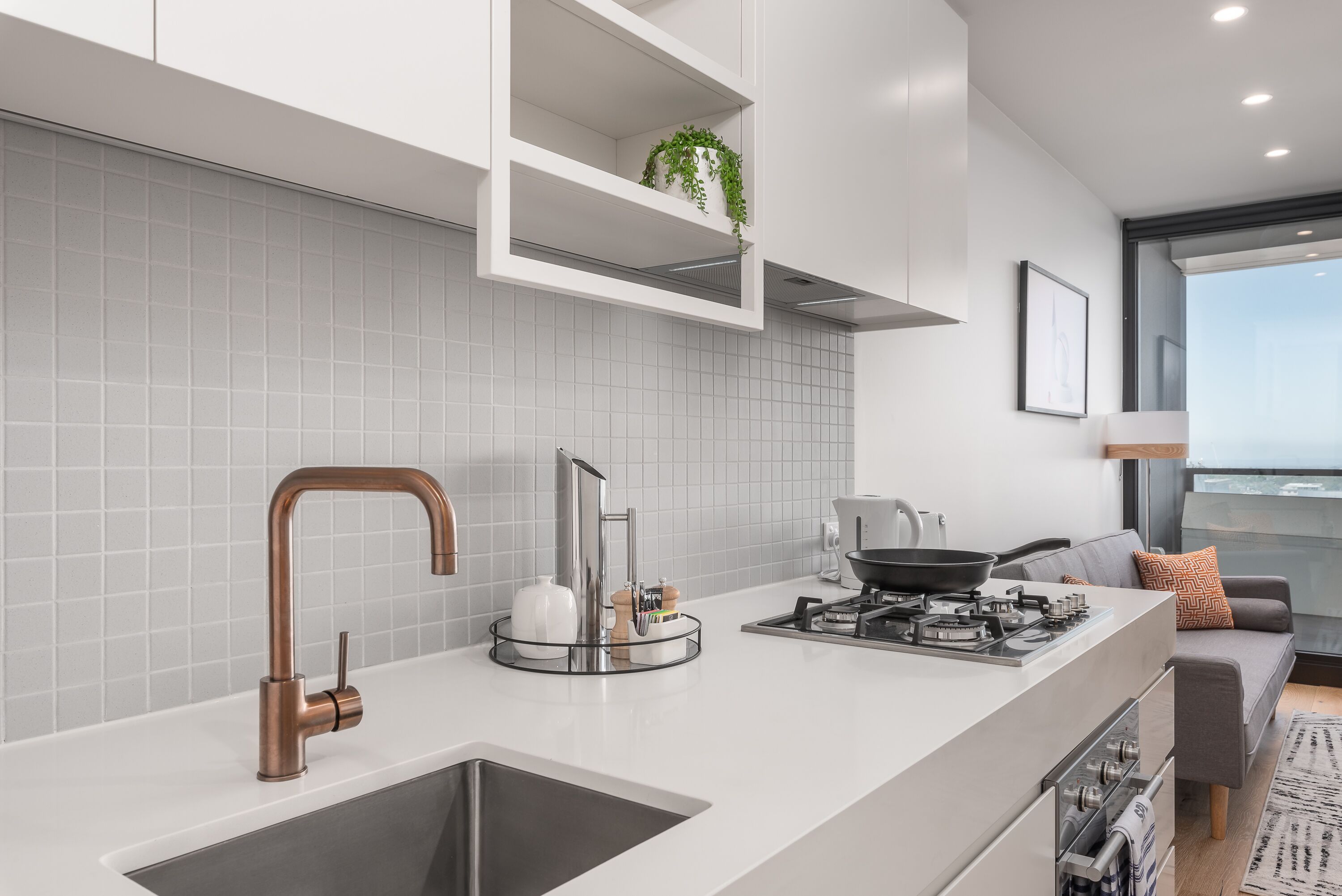 Une cuisine moderne dotée d’un robinet en cuivre, d’une cuisinière encastrée et d’un dosseret de carrelage gris.