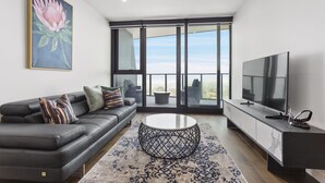 A modern living room with a black leather sofa, a round coffee table, and a large flat-screen TV. - Domi Serviced Apartments (Glen Waverley)