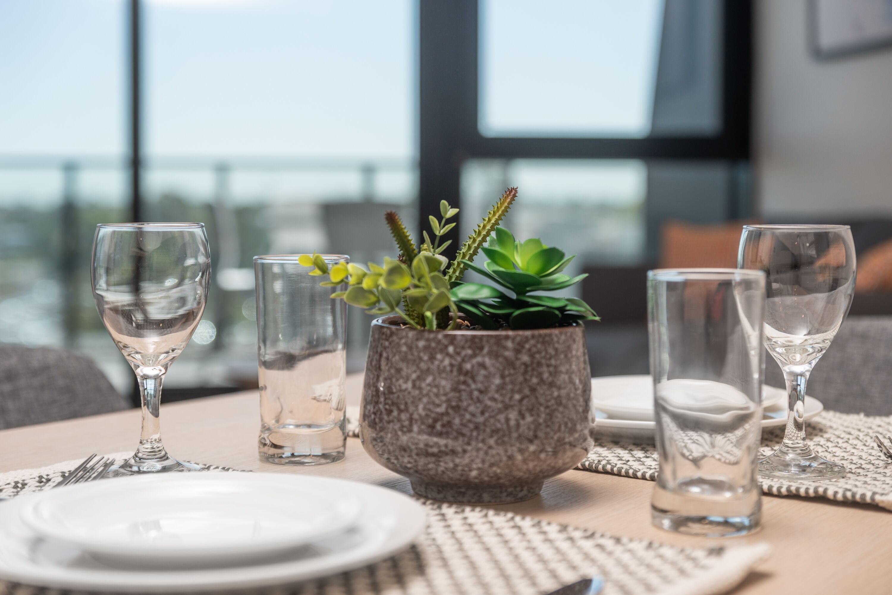 A dining table set with plates, glasses, and a potted plant.